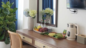 Ett hotellrum med ett skrivbord i trä, en stor spegel, en tv, en krukväxt, en vas med blommor och en kaffebryggare.