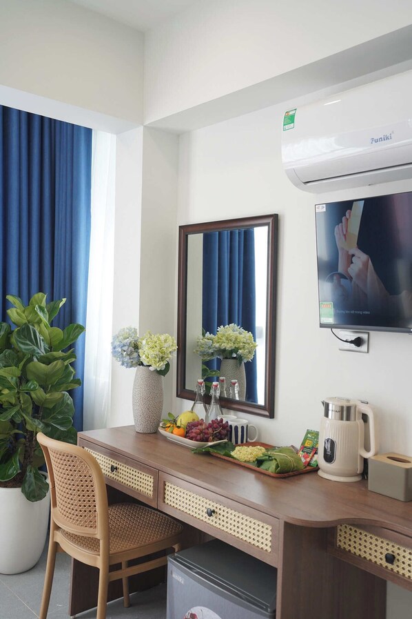 Ein Hotelzimmer mit einem Holztisch, einem großen Spiegel, einem Fernseher, einer Topfpflanze, einer Vase mit Blumen und einer Kaffeemaschine.