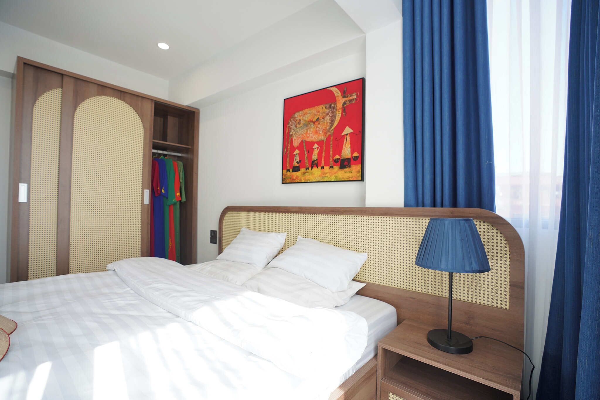 Une chambre d’hôtel avec un lit, une table de chevet, une lampe, une armoire et un tableau au mur.