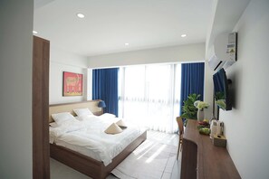 Une chambre d’hôtel moderne avec un grand lit, une table de chevet, un téléviseur fixé au mur et une fenêtre avec des rideaux.