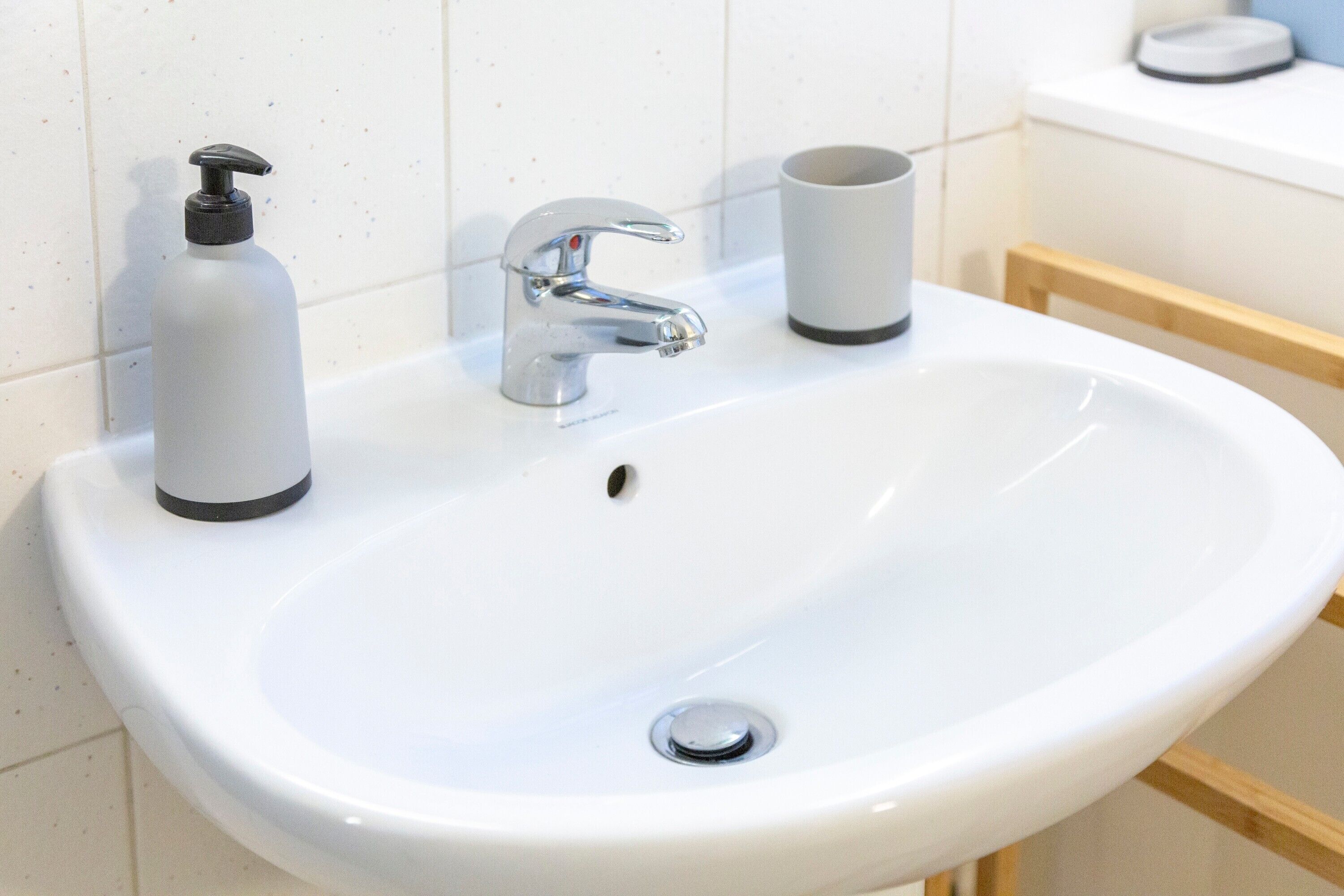 Een wit badkamermeubel met een chromen kraan, een zeepdispenser en een beker.
