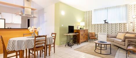 A modern living room with a sofa, a dining table with chairs, a TV, and a kitchen area with cabinets and a stove.