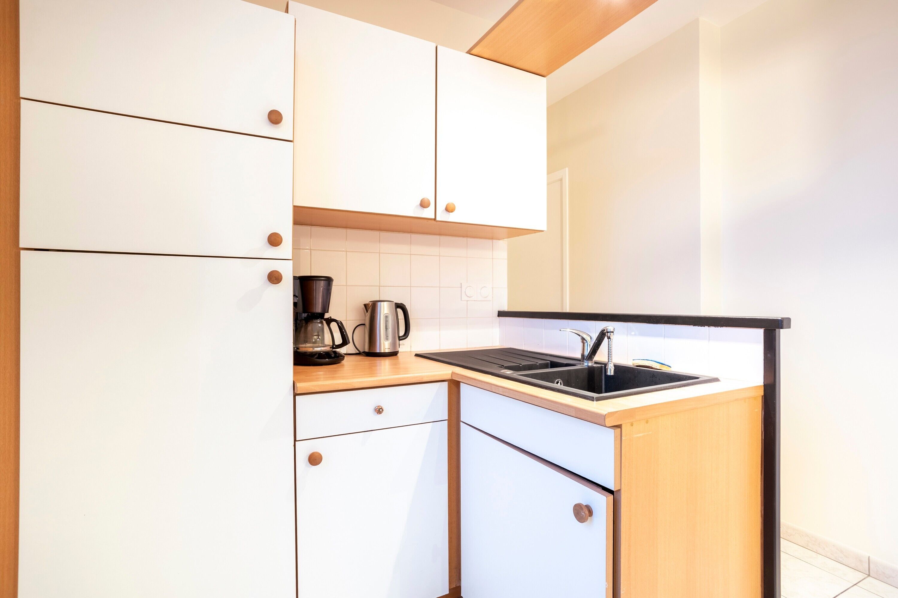 Een compacte keuken met witte kasten, een zwart aanrecht, een koffiezetapparaat en een spoelbak.