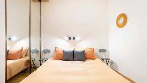 Een slaapkamer met een bed, twee stoelen, een klein tafeltje, een spiegel en een wandlamp.