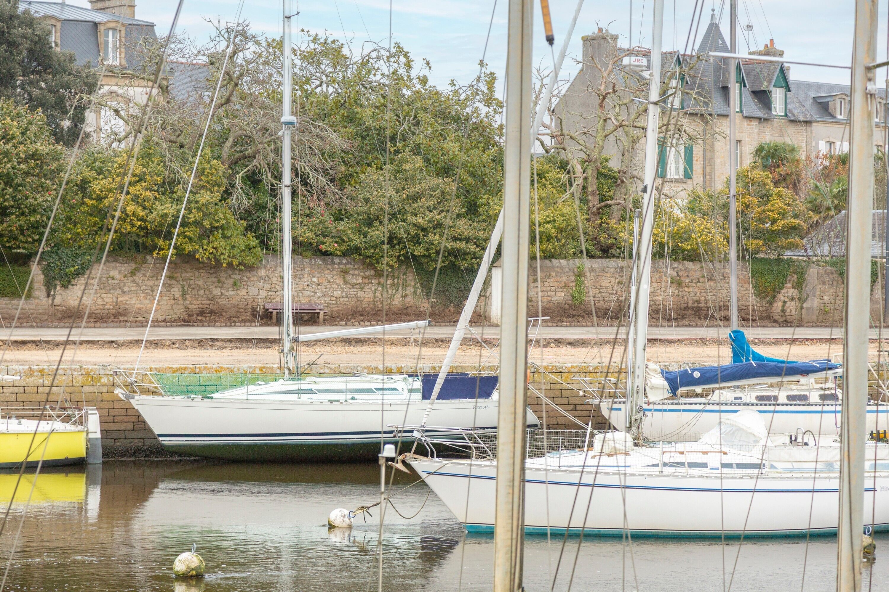 A marina with several boats docked, a stone wall, and a building in the background.