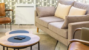 Een woonkamer met een beige bank, twee fauteuils, een salontafel en een witte radiator.