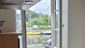 Een kanaalzicht vanuit een raam, met een gele boot en geparkeerde auto's.