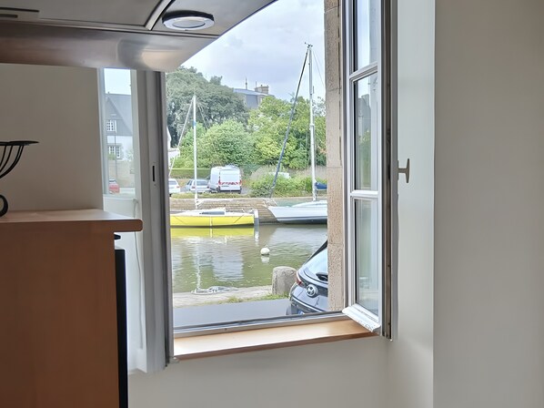 A window with a view of a canal, a yellow boat, and parked cars.