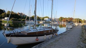 A marina with boats docked along a cobblestone waterfront, surrounded by buildings and trees. - Renovated Apartment in the Heart of Pont-l’Abbé – River View, Close to the Ocean (Pont l'abbé)