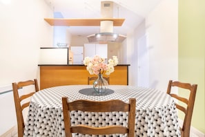 A dining table with a patterned tablecloth, wooden chairs, and a vase with flowers. - Renovated Apartment in the Heart of Pont-l’Abbé – River View, Close to the Ocean (Pont l'abbé)
