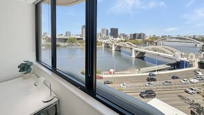 A room with a large window overlooking a cityscape, including a river and a bridge. - River View Sanctuary - Walk to CBD & South Bank (Brisbane City)