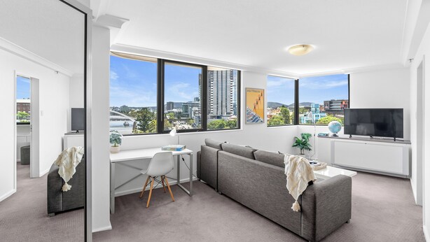 A modern living room with a grey sofa, a desk, and a TV. - River View Sanctuary - Walk to CBD & South Bank (Brisbane City)