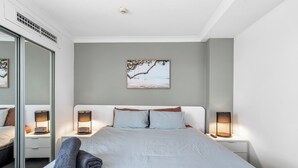 A modern bedroom with a large bed, two bedside tables with lamps, a wall-mounted picture, and a sliding glass door. - River View Sanctuary - Walk to CBD & South Bank (Brisbane City)