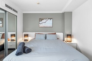 Ein modernes Schlafzimmer mit einem großen Bett, zwei Nachttischen mit Lampen, einem Wandbild und einer Schiebeglasdoor.