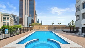 A rooftop swimming pool with a wooden deck, surrounded by a black metal fence, and high-rise buildings in the background. - River View Sanctuary - Walk to CBD & South Bank (Brisbane City)