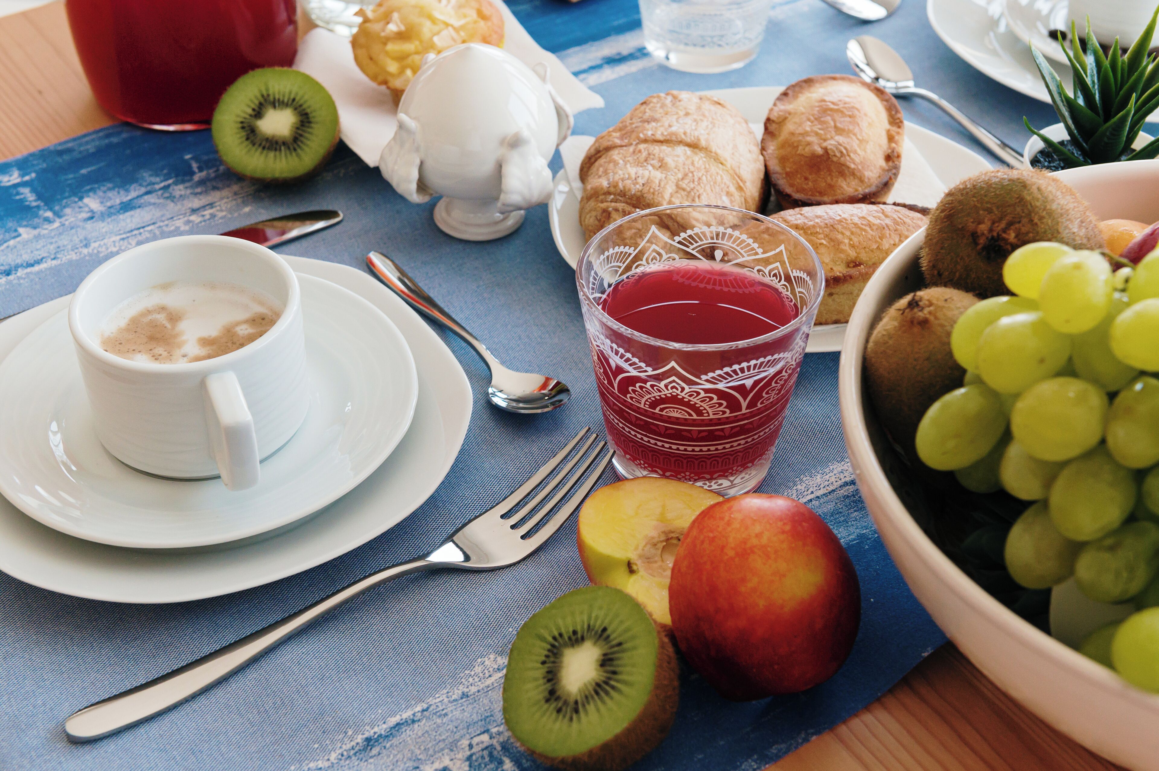 A breakfast setting with a cup of coffee, a glass of juice, a bowl of grapes, and various pastries on a table.