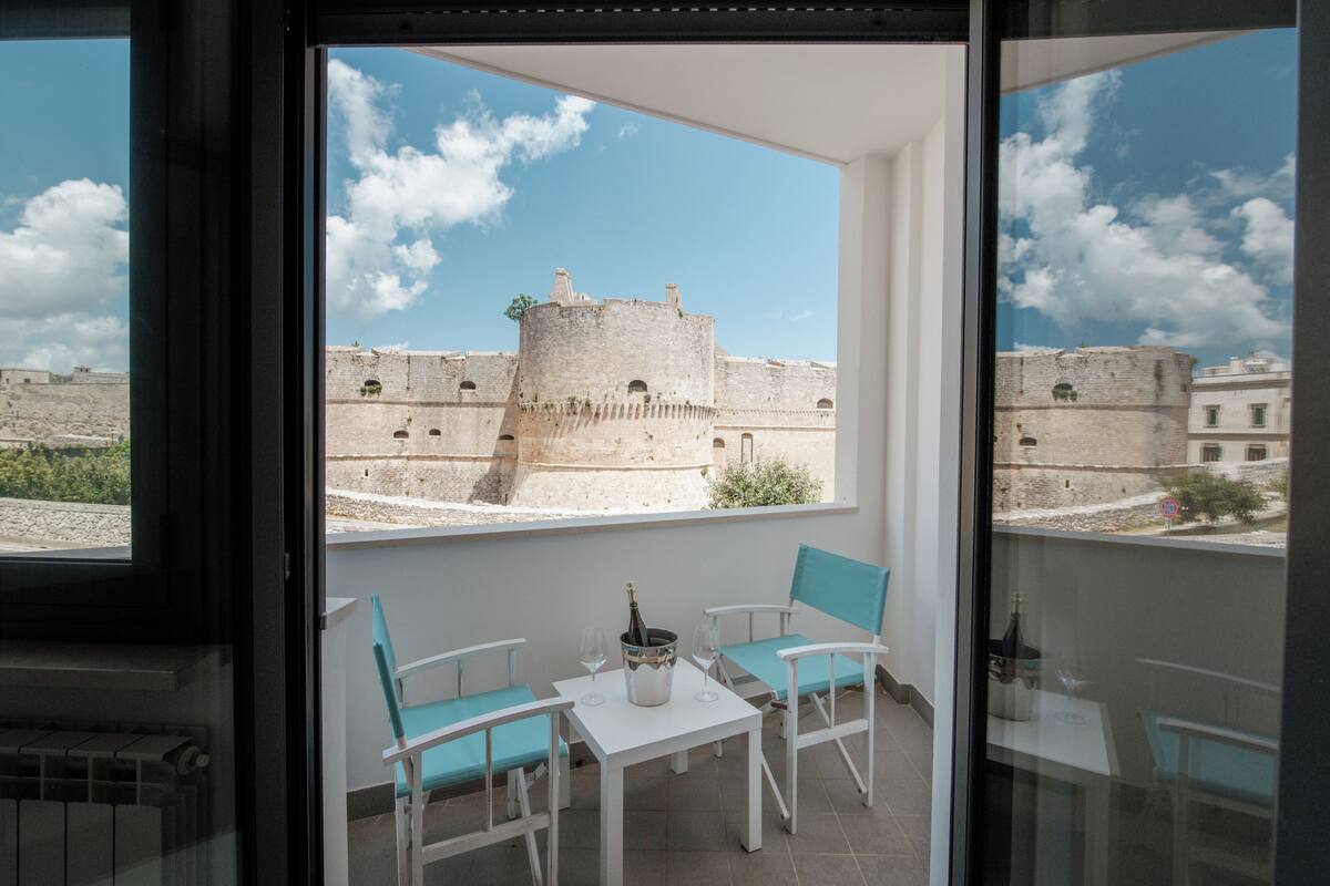 Un balcon avec une table et des chaises, une bouteille de champagne et une vue sur un ancien mur de pierre.