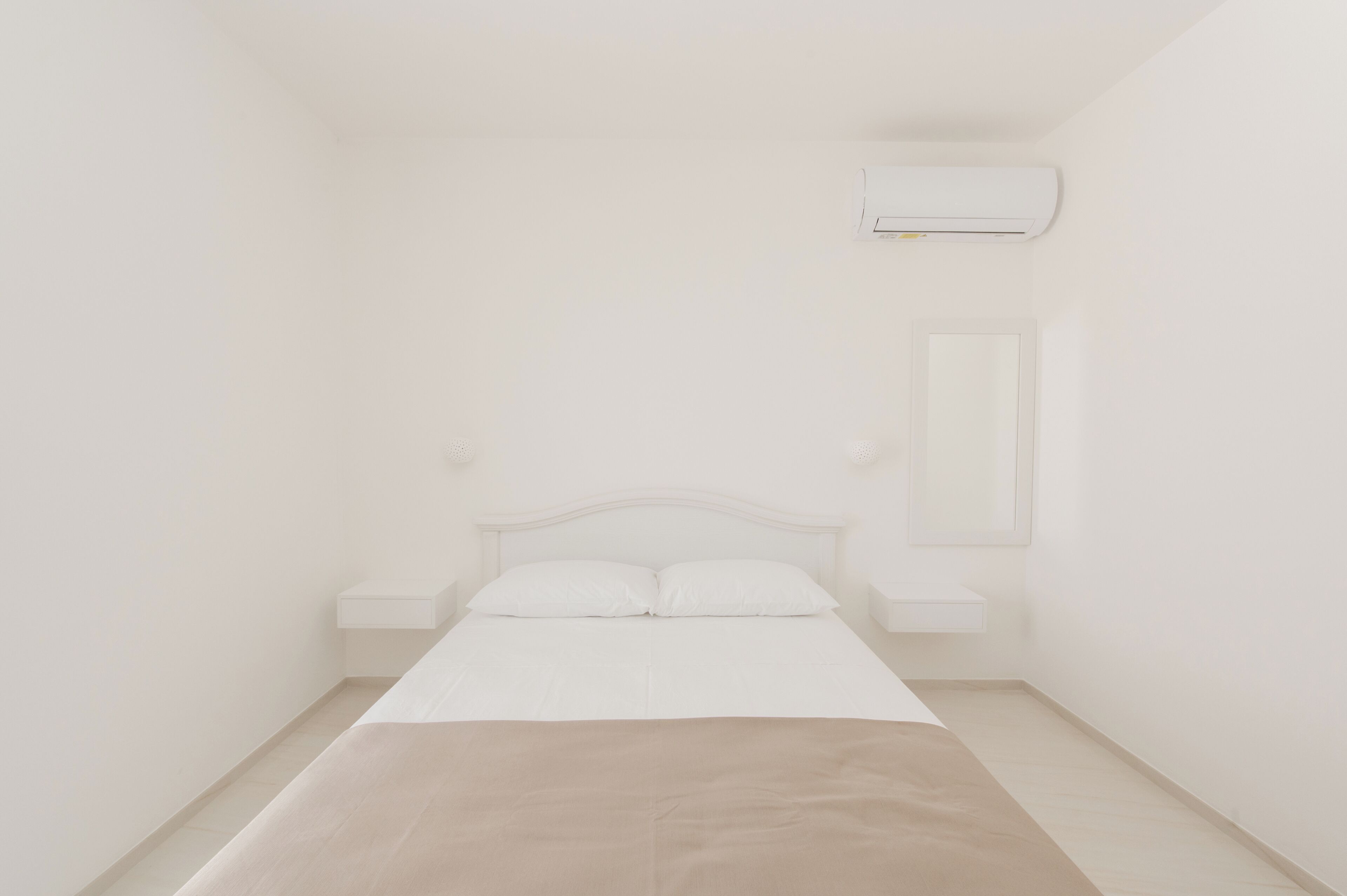 A minimalist bedroom with a single bed, a nightstand, a wall-mounted air conditioning unit, and a small bedside table.