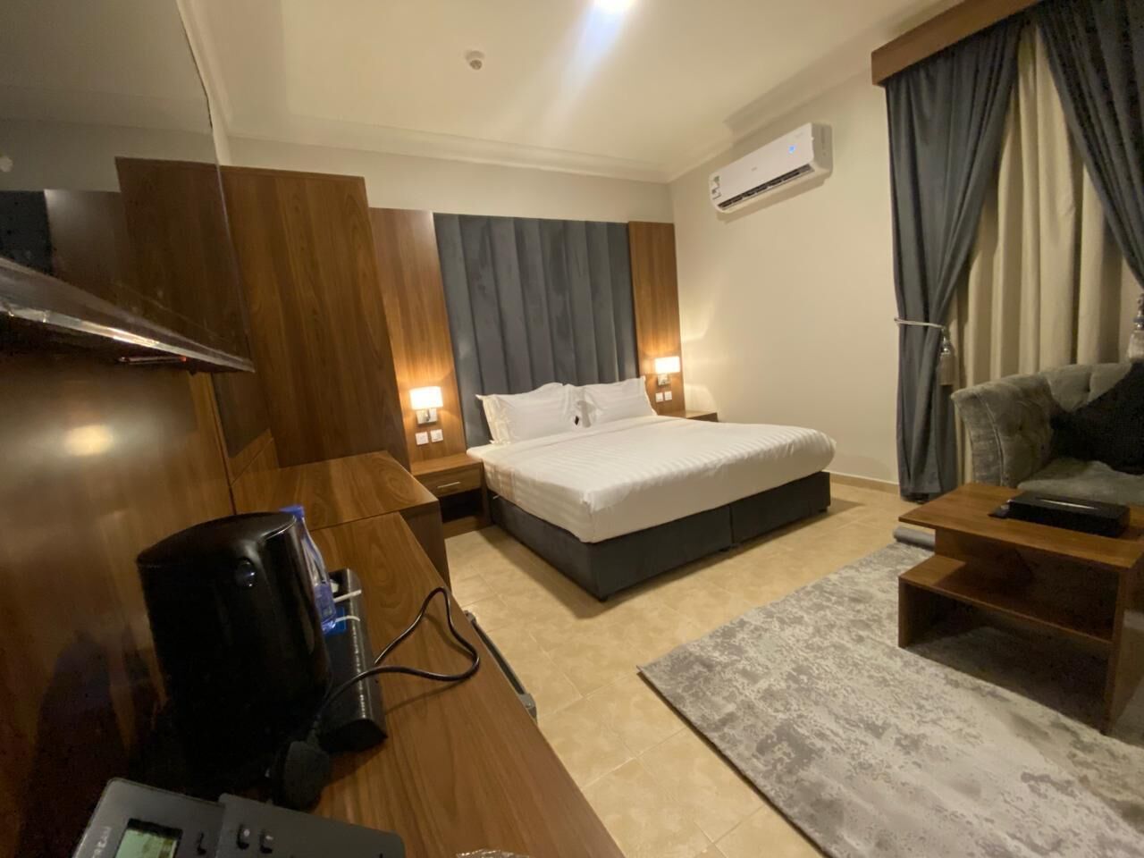 A modern hotel room with a bed, bedside tables, a desk, and a TV.