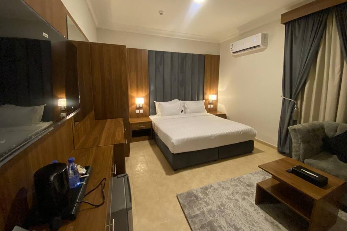 A hotel room with a bed, bedside tables, a TV, a desk, and a couch.