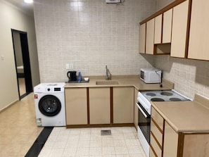 A compact kitchen with a washing machine, microwave, and stove. - Manazel Al Khaleej Hotel Apartments (Dammam)