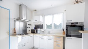 A modern kitchen with white cabinets, a gas stove, a microwave, and an oven. - Family Vacation Home in Bénodet (bénodet)