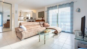 A living room with a sofa, a glass coffee table, a television, and a kitchen in the background. - Family Vacation Home in Bénodet (bénodet)