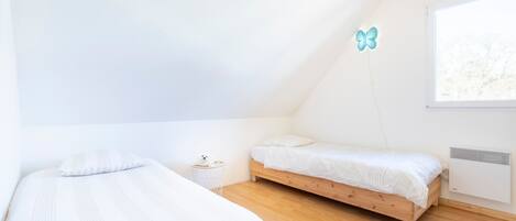 A bedroom with two beds, a small bedside table, a window, and a wall-mounted air conditioner.