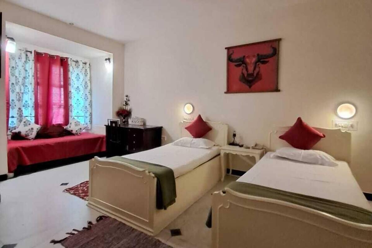 Ein Hotelzimmer mit zwei Betten, einem roten Vorhang, einem Gemälde mit Stier-Motiv und einem roten Kopfkissen auf einem Bett.