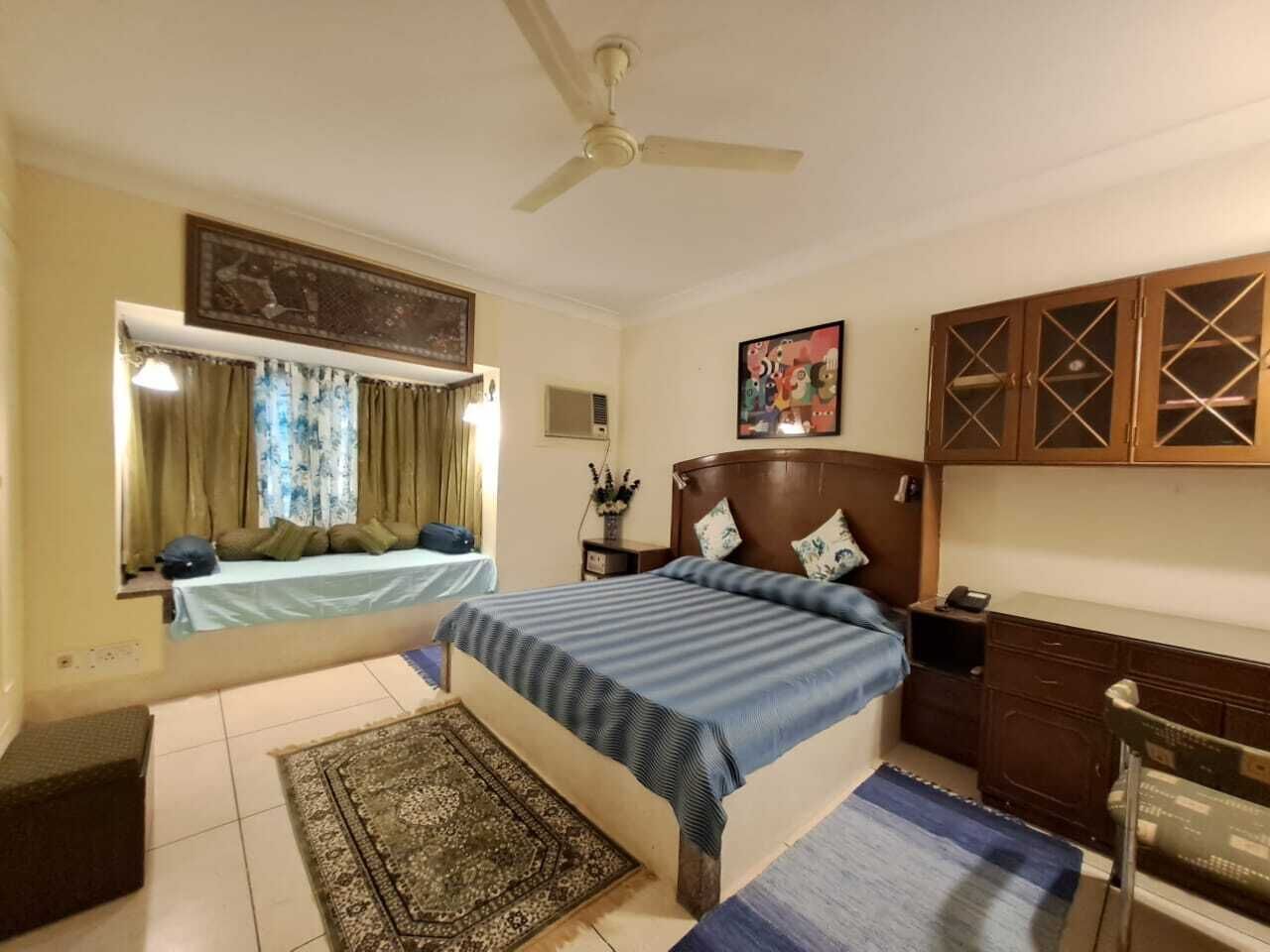 Un dormitorio con cama, ventilador de techo, mesita de noche, cómoda y ventana con cortinas.
