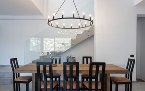 Un espace de salle à manger moderne, doté d’une grande table en bois, de six chaises noires et d’un lustre circulaire original.