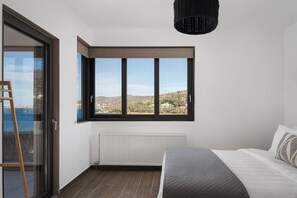 Une chambre avec une grande fenêtre, un radiateur et un lit recouvert d’une couette matelassée.