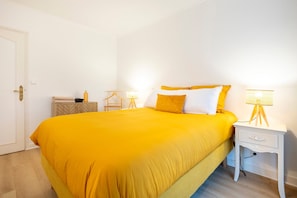 Een kamer met een bed, nachtkastje, lamp en een deur.