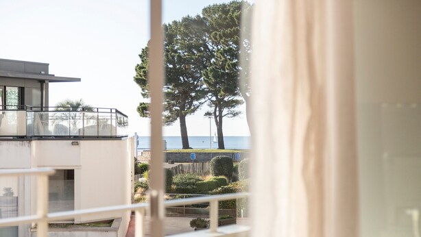 Vista dalla finestra su un edificio con un balcone, uno spazio verde e alberi.