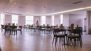 A spacious dining area with multiple tables and chairs, large windows, and a high ceiling with recessed lighting.