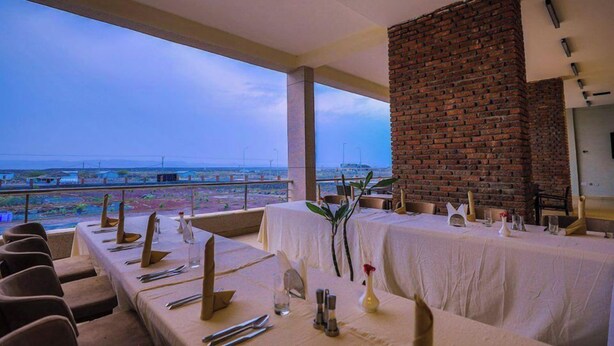 A restaurant with a long table set for dining, a brick wall, and a view of the landscape.