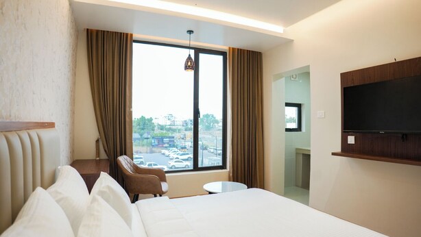 Habitación de hotel con una cama grande, una silla, una mesita, un televisor y una ventana con cortinas.