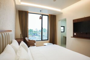 A hotel room with a large bed, a chair, a small table, a TV, and a window with curtains.