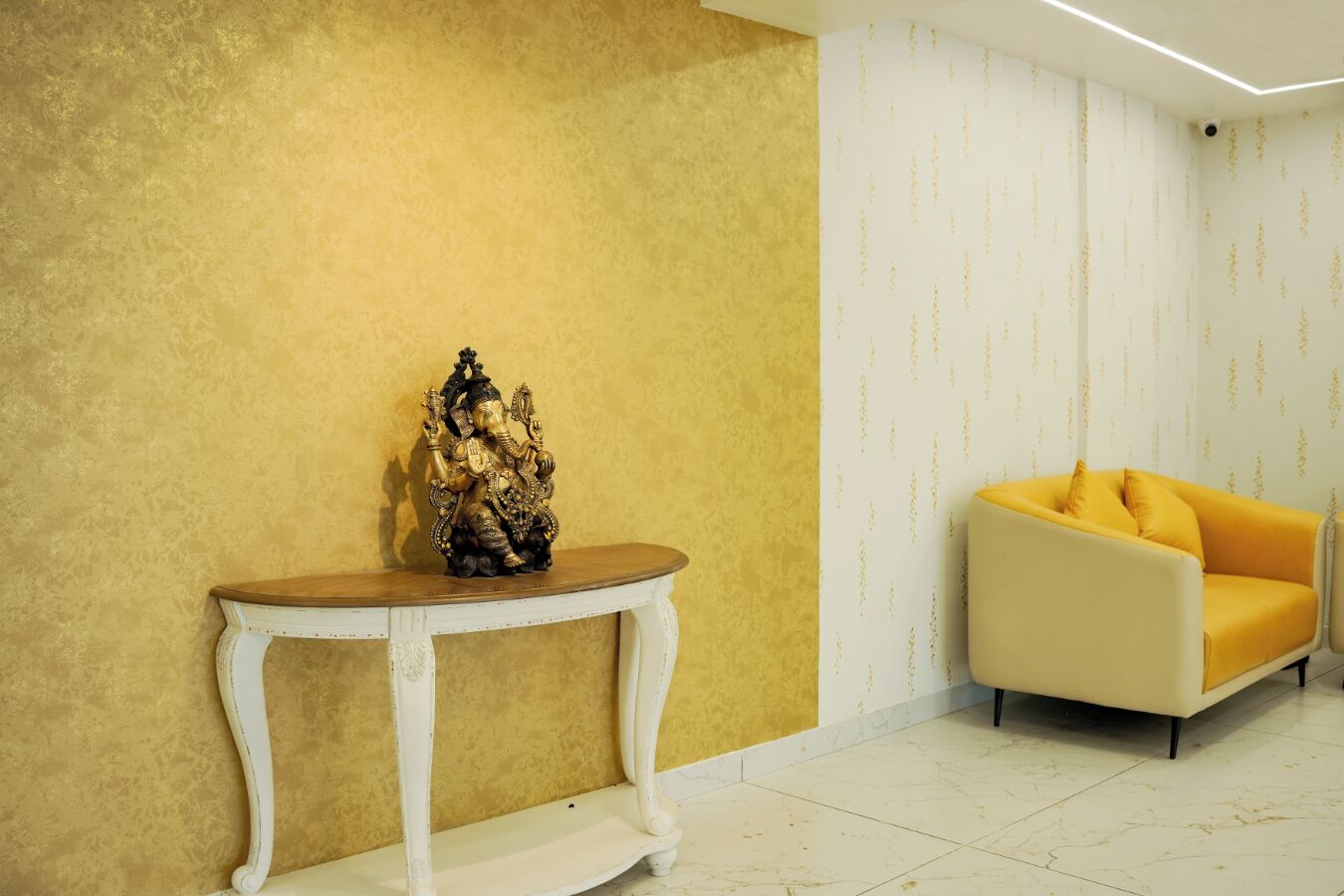 A room with a yellow textured wall, a white console table with a statue, and a yellow sofa.