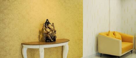 A room with a yellow textured wall, a white console table with a statue, and a yellow sofa.