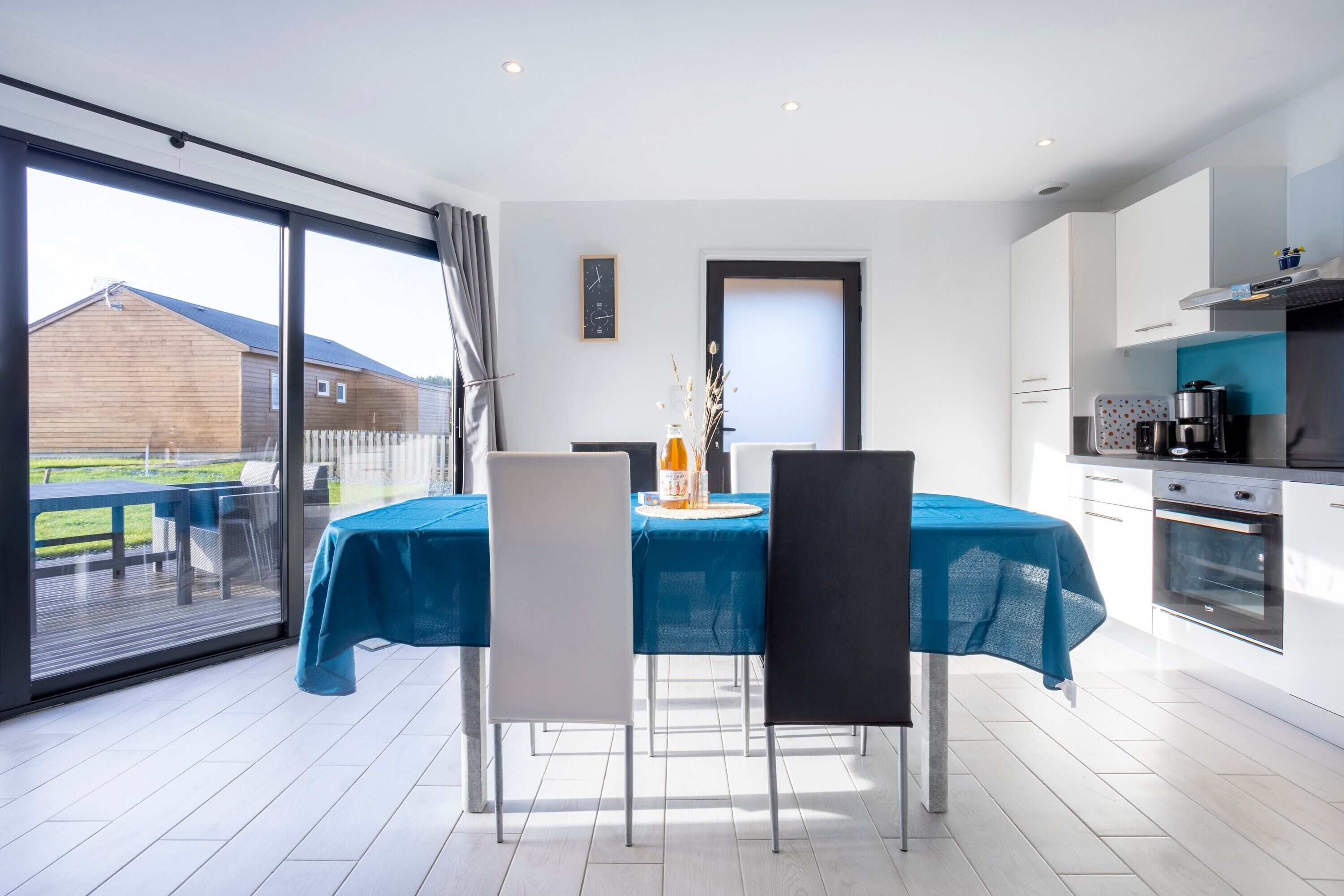 A modern kitchen with white cabinets, a dining area with a blue tablecloth, and a large sliding glass door leading to an outdoor patio.