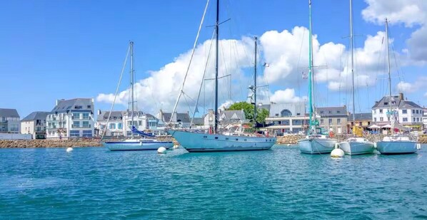 A marina with several sailboats docked, a waterfront promenade, and buildings with a coastal architectural style.