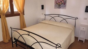 Un letto con struttura metallica, un comodino, una lampada a muro e un quadro con fiori.
