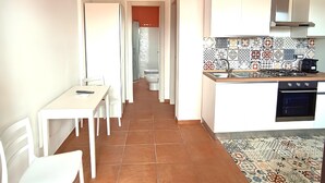 Una cucina compatta con mobili bianchi, zoccolo in piastrelle e zona pranzo con tavolo e sedie.