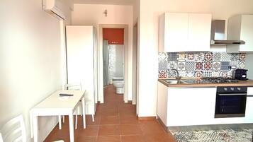 Una cucina compatta con mobili bianchi, zoccolo in piastrelle e zona pranzo con tavolo e sedie.