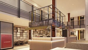 A modern indoor space with a central counter, seating areas, and a mezzanine level with a staircase. - Beezie Hotel (Palembang)