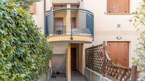 A narrow alleyway with a curved balcony, a wooden gate, and a potted plant.