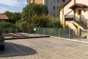 A residential building with a paved driveway, a staircase, and a fenced garden area.