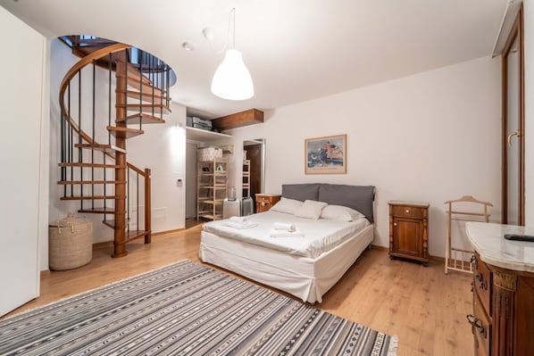 A bedroom with a wooden spiral staircase, a bed with white bedding, a hanging light fixture, and a wooden cabinet.