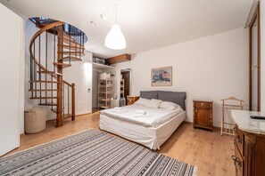 A bedroom with a wooden spiral staircase, a bed with white bedding, a hanging light fixture, and a wooden cabinet.
